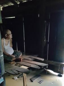 An older person sitting inside a wooden house in Burma